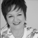 Black and white headshot of Janette Dalgliesh, wearing a bold floral print shirt and a pearl necklace