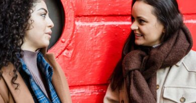 two women in their twenties sitting in front of a red wall apparenty talking
